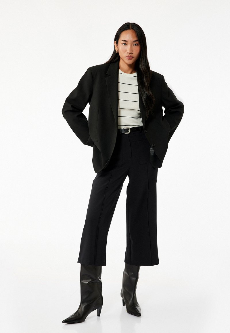 Sort oversized blazer over en stribet, lys top, parret med sorte cropped bukser og knæhøje spidse støvler.