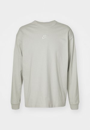 T-shirt a maniche lunghe grigio chiaro in cotone. Presenta un collo rotondo e un piccolo logo Nike bianco sul petto. Texture liscia e design casual.