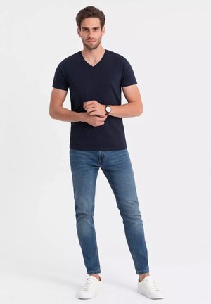 Camiseta de cuello en V de color navy, de algodón ligero, combinada con jeans ajustados azules y zapatillas blancas, creando un look casual con un detalle mínimo.