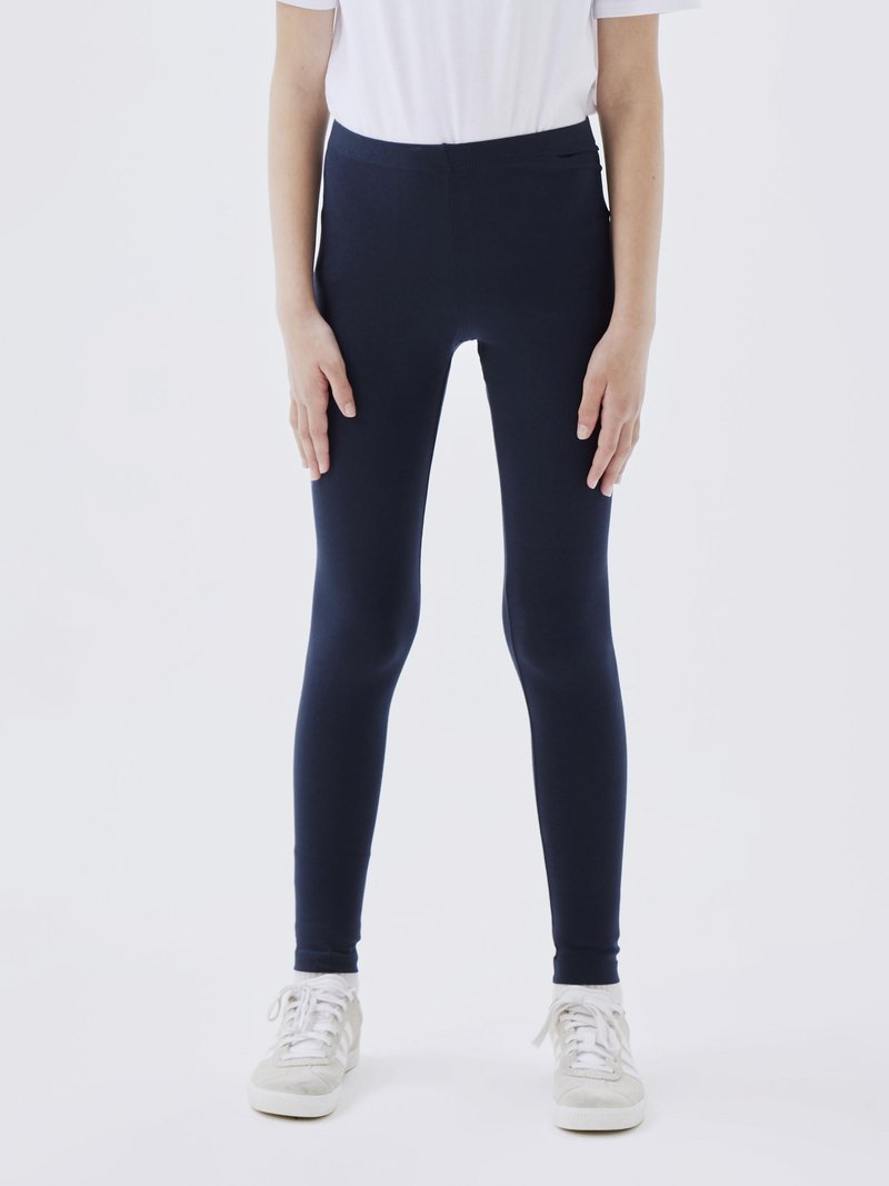 Mørkeblå leggings laget av elastisk materiale, med høy midje og en tettsittende design, kombinert med lysegrå joggesko.