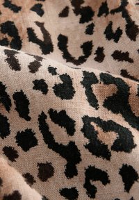 Látka s leopardím vzorem na béžovém podkladu, která má černé a tmavě hnědé skvrny. Povrch vypadá tkaný a je mírně hrubý.