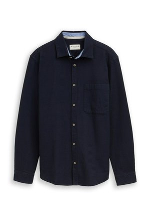 Granatowa koszula na długi rękaw zapinana na guziki, z kieszenią na piersi i jasnoniebieską podszewką kołnierza wewnętrznego, ułożona płasko na białym tle.