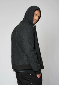 Veste bomber en suede noir avec une capuche grise, des poignets et un ourlet côtelés, des poches latérales et une surface légèrement texturée.