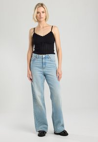 Black ribbed tank top with scalloped edges, paired with light blue wide-leg jeans with a slight fade, and black platform shoes.