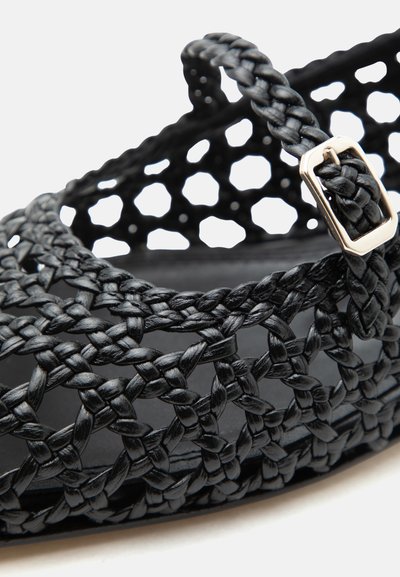 Mustast punutud nahast sandaali lähivaade, millel on avatud võrgustiku disain ja hõbedane pandlarihm.