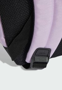 Lila och svart ryggsäck i hörnet med texturerad nätväv, slät material och ett säkert justerbart bälte med varumärkesinramat hårdvara.