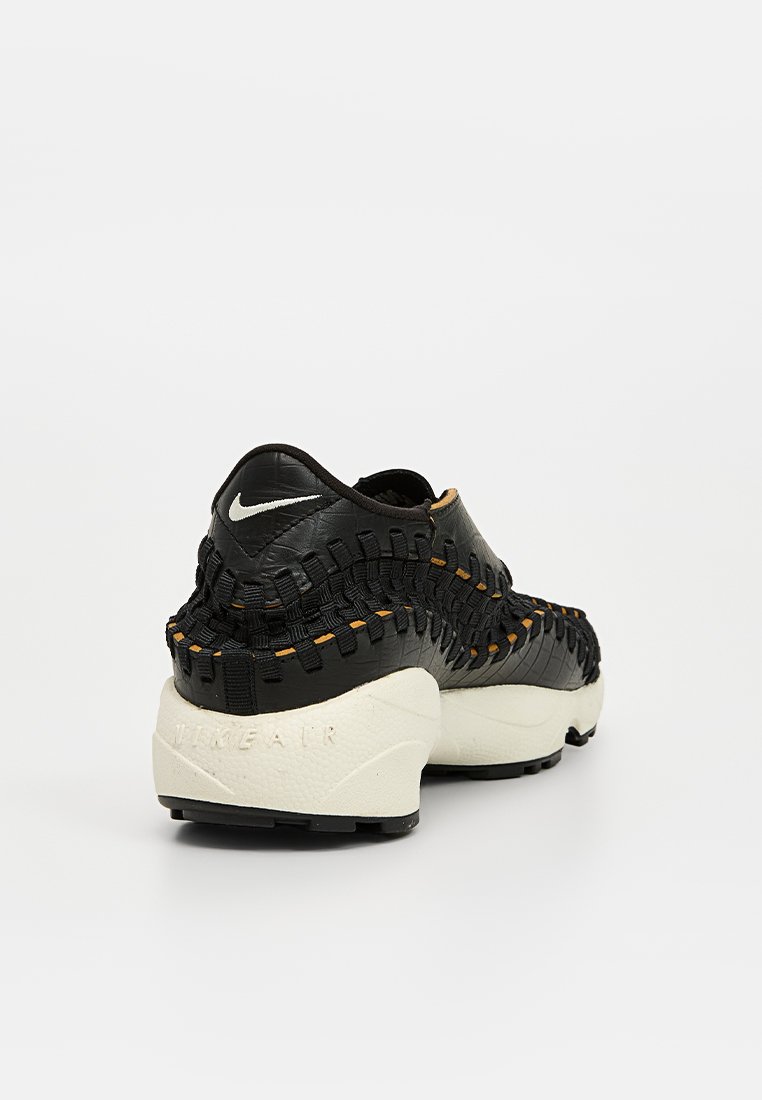 Baskets noires tissées avec une semelle blanche épaisse, présentant un dessus en cuir texturé et un petit logo blanc à l'arrière.
