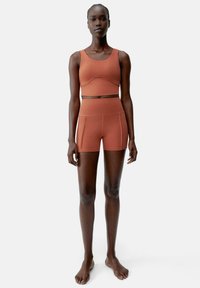 Sport-BH i rostfärg med matchande högmidjade shorts i mjukt, elastiskt material. Enkelt design utan synliga mönster eller detaljer.
