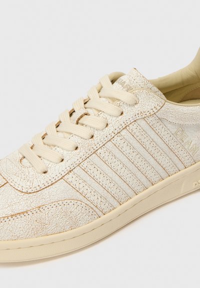 Baskets beige clair avec un dessus en cuir texturé, présentant des rayures horizontales et un laçage. Semelle en caoutchouc durable avec un design simple.