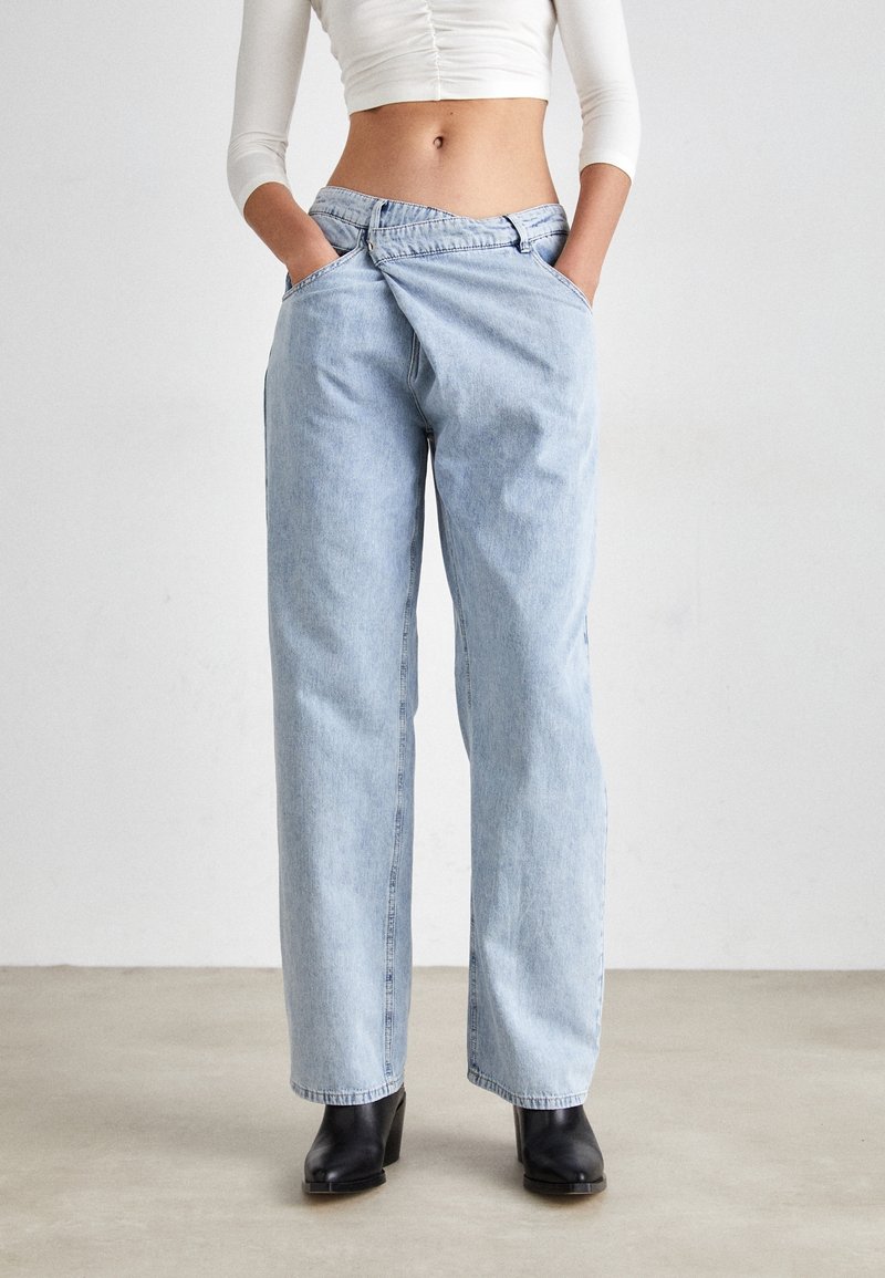Pantalones de mezclilla de tiro alto en azul claro, con un corte relajado, que cuentan con dos bolsillos laterales y una cinturilla plana, combinados con botas de tacón negras.