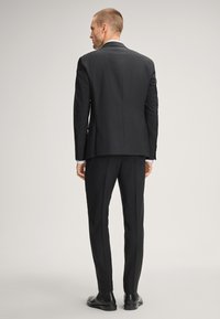 Schwarzer Anzug mit maßgeschneiderter Passform, feiner Textur, scharfen Revers und passenden Hosen, kombiniert mit schwarzen Anzugschuhen.