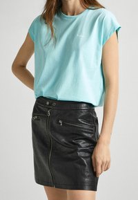 Ljusblå bomullströja med rullade kap ärmar, i kombination med en åtsittande svart läderkort kjol med dragkedjefickor och frontknäppning.