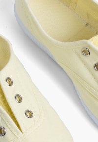 Płótniaki w jasnym żółtym kolorze z białymi gumowymi podeszwami, z metalowymi oczkami i kontrastowymi detalami haftu.