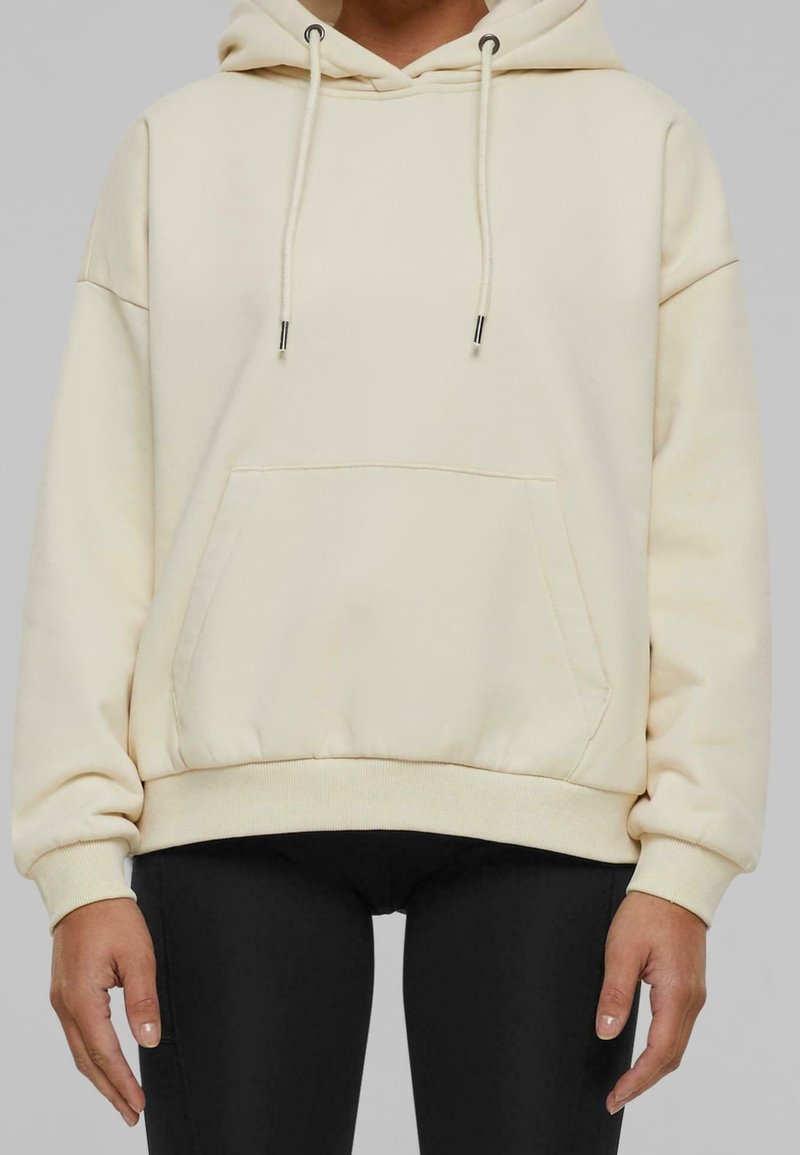 Hoodie crème avec poche kangourou, capuche à cordon et poignets côtelés. Tissu doux avec une coupe décontractée. Associé à des leggings noirs.