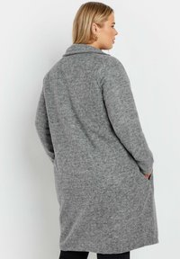 Grå ullblandad kappa med sjalkrag, långa ärmar, sidofickor och knälång skärning, med ett mjukt, texturerat tyg.