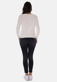 Maglione bianco a maniche lunghe con scollatura rotonda, aderente in vita, abbinato a jeans skinny scuri e sneakers bianche.