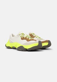 Sneaker con tomaia in suede beige e marrone, suola gialla neon e lacci coordinati. Forma arrotondata con suola in gomma testurizzata.