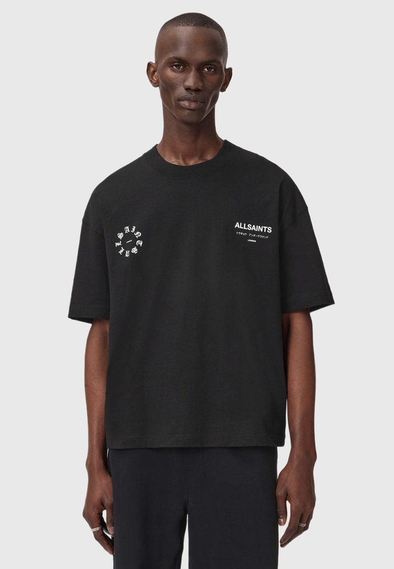 Mustard värvi puuvillane t-särk lühikeste varrukatega, ümmargune kaelus, esiküljel graafilised prindid ja mugav lõige. Tekst sisaldab "ALLSAINTS" logo ja kujunduselemente.