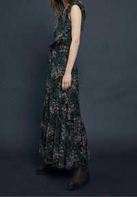 Robe maxi florale de couleur vert foncé avec des motifs roses et bleus, dotée d'un corsage ajusté, d'un ourlet volanté et d'une taille ceinturée. Associée à des bottes noires.