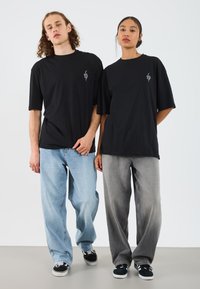 Sorte oversized t-skjorter med liten grafikk på brystet, kombinert med lyseblå og mørkegrå baggy jeans. Sneakers fullfører det avslappede utseendet.