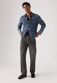 Sinine teksasärk kahe rinnataskuga, kantud musta särgi peal; kombineeritud hallide teksade ja mustade kingadega; lõtv istuvus.