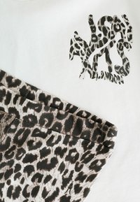 Camiseta con logo de estampado de animal en negro sobre tela blanca; combinada con tela de estampado de leopardo en tonos marrón apagado y negro.
