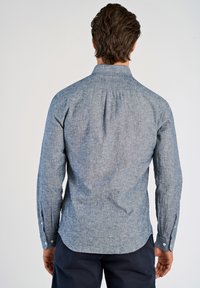 Camisa de manga larga con cuello en una tela texturizada de color azul claro. Cuenta con puños abotonados y un pliegue en la parte posterior para mayor movilidad.