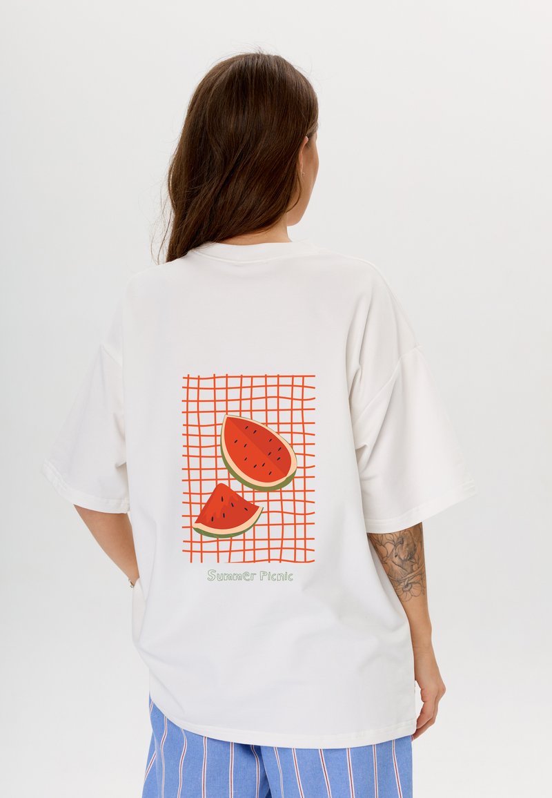 Witte oversized t-shirt met een rood roosterontwerp, twee schijven watermeloen en de tekst "Zomer Picknick" onderaan.