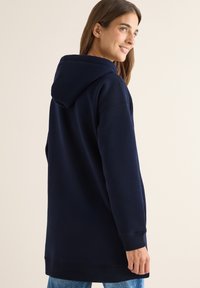 Felpa navy con un design spazioso, tessuto strutturato e una grande tasca posteriore. Presenta un cappuccio con cordino e polsini a coste.