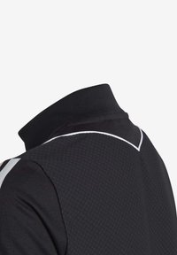 Close-up van een zwart gestructureerd polo-shirt met een geribbelde kraag en witte pipingdetails op de schouder en rug.