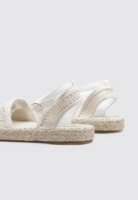 Sandalias trenzadas blancas con un diseño texturizado, una suela de yute trenzada y una correa ajustable con un detalle de hebilla en tono dorado.