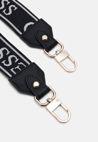 Černý textilní popruh s koncovkami z texturované kůže, vybavený stříbrnými kovovými sponami a bílým logem potištěným po celé délce.