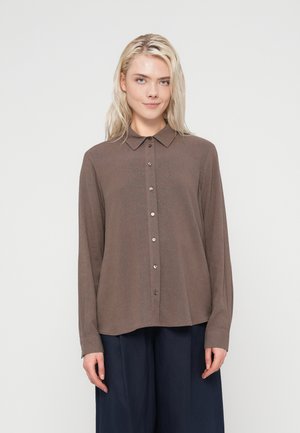 Brun langærmet skjorte med knapper og krave, der har en blød tekstur og let buet kant. Knapperne er runde og metalliske.