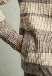 Stickad tröja med horisontella ränder i beige och taupe. Har ribbade ärmslut och nederkant, tillverkad av mjukt strukturerat material.