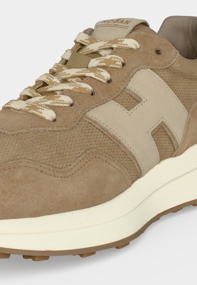 Baskets en daim beige avec des lacets beige et blancs à motifs, grand "H" cousu sur le côté et semelle blanche rembourrée.