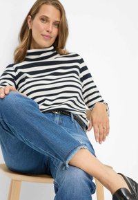 Top lavorato a maglia a righe bianche e nere con collo alto, abbinato a jeans blu strappati con orli sfrangiati e mocassini neri.