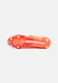 Scarpa da football con suola in gomma arancione brillante, dotata di numerosi tacchetti, parte superiore liscia e una striscia bianca centrale.