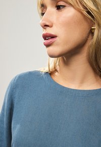 Blue linen garment with a round neckline. Close-up view highlighting smooth texture and subtle fabric detailing. Simple design without patterns.