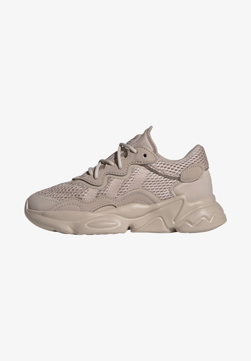 Light beige sneaker featuring a mesh upper, textured accents, curved design, and a chunky sole with wavy shapes. Lace-up closure.