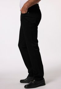 Svarta denimbyxor med slim fit, som har framfickor och en slät yta. Bärs med svarta skor, sidovy visas.