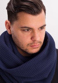 Navy blue knitted infinity scarf featuring a textured rib pattern, wrapped around the neck, with a smooth finish and subtle hardware detail.