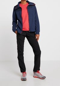 Námořnická zipová bunda s červenými akcenty, červené tričko, černé kalhoty a šedo-červené tenisky. Hladká tkanina, sportovní střih, funkční design.