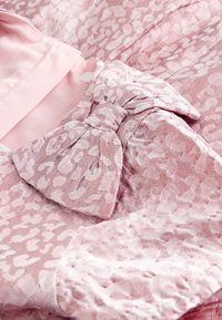Tissu de robe rose avec un motif léopard, présentant un détail de nœud texturé près de l'encolure. Doublure lisse en rose tendre.