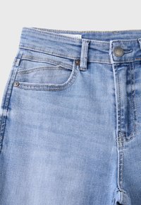 Jean en denim bleu clair avec poches avant, passants pour ceinture, bouton en métal et coutures apparentes sur un fond clair uni.