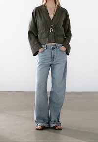 Oliven grøn cropped top med V-hals og forlommer, parret med lyseblå vidde bukser, suppleret med brune sandaler.