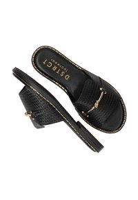 Sandales tissées noires à enfiler avec une semelle plate, comportant un accent en métal doré et des détails cousus le long des bords.