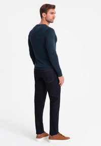 Marinblå långärmad skjorta, formad design, ribbade manschetter; kombinerad med mörka jeans och bruna sneakers, med en ren estetik och minimala detaljer.