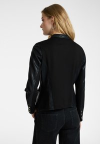 Giacca nera con tessuto aderente e maniche in pelle. Rifinita con bottoni dorati sui polsini, presenta un design strutturato e una finitura testurizzata.