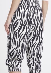 Pantaloni a stampa zebra in bianco e nero, con cintura elastica, polsini arricciati alle caviglie e un tessuto leggero e testurizzato.