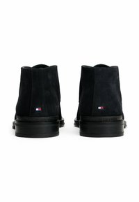 Un paio di stivaletti neri in suede con tacco a blocco, vista posteriore che mostra il piccolo logo di Tommy Hilfiger su ciascun tacco.